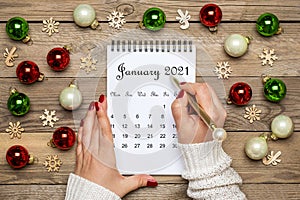 Female hand holds pen, open Calendar January 2021, Christmas decor on wooden table