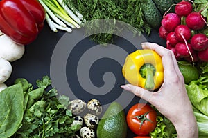 Female hand holds pepper. Composition with different fresh organic fruits and vegetables.