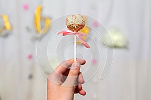 Female hand holds pop cakes on pastel background. White chocolate cake pop decorated with colorfull confectionery sprinkles. Party