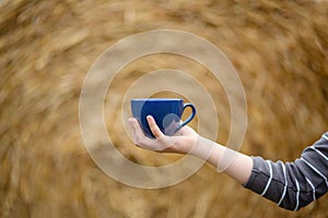Female hand holds a porcelain cup of coffee on a natural background. Selective focus on the cup