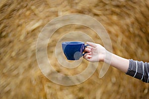 Female hand holds a porcelain cup of coffee on a natural background. Selective focus on the cup