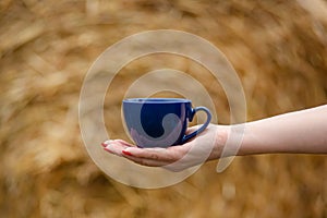 Female hand holds a porcelain cup of coffee on a natural background. Selective focus on the cup