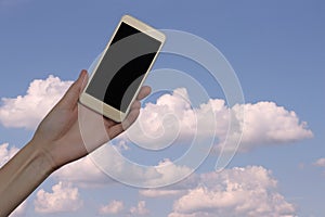 Female hand holds a smartphone on a background of the sky with clouds. Girl holds a mobile phone with a blank screen