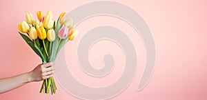 Female hand holds spring bouquet of tulips on a pink background