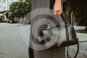 Female hand holds a square leather bag. Street look of a business woman. An independent strong business lady left the office