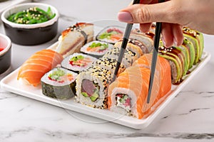 Female hand holds a sushi roll with chopsticks. Sushi rolls set served on a white plate.