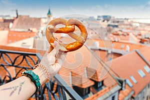 Female hand holds a traditional bakery and a pretzel delicacy against the background of the historic center of the European city