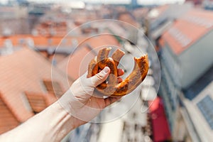 Female hand holds a traditional bakery and a pretzel delicacy against the background of the historic center of the European city
