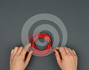 Female hand holds twisted cable for charging mobile devices in a red textile wrapper on a black background