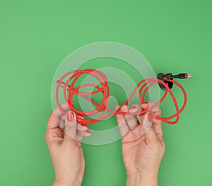 Female hand holds twisted cable for charging mobile devices in a red textile wrapper on a green background