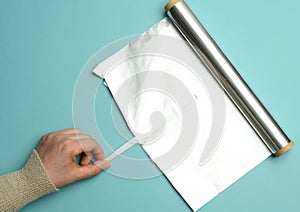 Female hand holds an unfolded roll of gray foil on a blue background