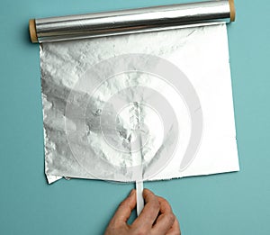 Female hand holds an unfolded roll of gray foil on a blue background