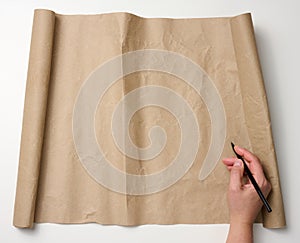 Female hand holds wooden pencil over brown paper roll on white table. Place to write text, list