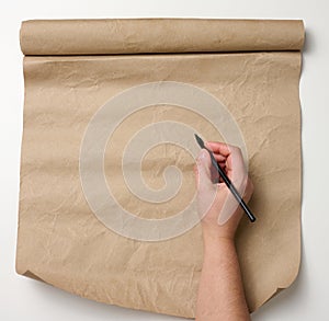 Female hand holds wooden pencil over brown paper roll on white table. Place to write text, list