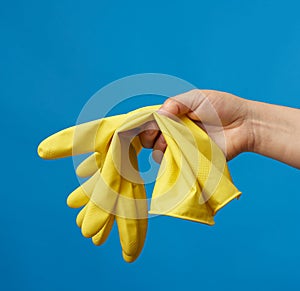 Female hand holds yellow  rubber gloves for cleaning, blue background