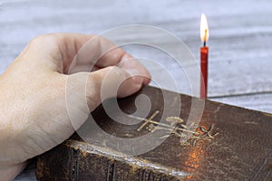 Female hand on holy bible dook and burning red church candle behind