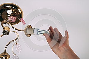 Female hand inserts a light bulb into the threaded socket. Installation of household LED lamps of corn type, in the lamp holder,