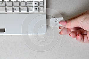 A female hand inserts a white compact SD card into the corresponding input in the side of the white netbook. Woman uses modern te