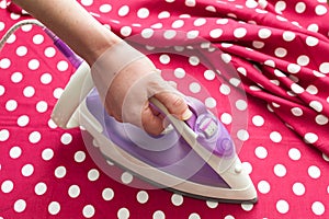 Female hand ironing clothes top view during housework. Close-up of maid hand ironing clothes on ironing board at home.