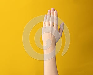 Female hand isolated showing five fingers on yellow background