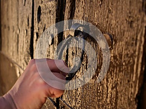 Female hand knocks on a round metal beater on a wooden old door