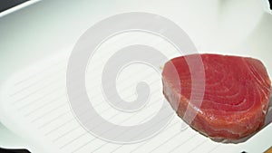 Female hand leaving raw tuna steak to fry in a ribbed white pan, 4K close up