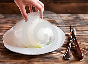 Female hand lifts to up cloche from a plate with hot food at re