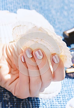 Female hand with light purple nail design with seashells decoration.