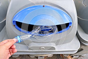 A female hand littering a plastic bottle of drinking water in a recycled trash bin at the park for cleaning environment concept