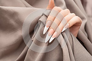 Female hand with long french nail design. Long french nail polish manicure. Woman hand on beige fabric background