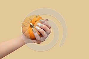 Female hand with long nail design. Glitter gold and white nail polish manicure. Female hand with perfect manicure hold pumpkin