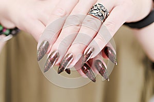 Female hand with long nails and a bottle of green brown nail polish