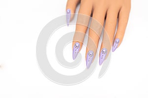 Female hand with long nails with glitter nail polish. Long purple nail design with rhinestones. Women hand with sparkle manicure
