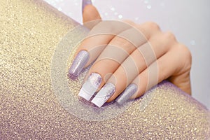 Female hand with long nails with glitter nail polish. Long purple nail design. Women hand with sparkle manicure on glitter