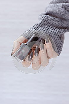 A female hand with long nails holds a bottle with a grey nail polish