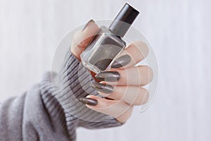 A female hand with long nails holds a bottle with a grey nail polish