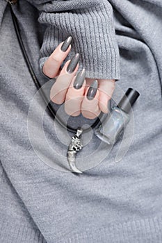 A female hand with long nails holds a bottle with a grey nail polish