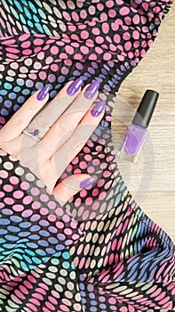 Female hand with long nails and pink fuchsia manicure holding a bottle