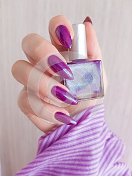 Female hand with long nails and pink manicure holding a bottle