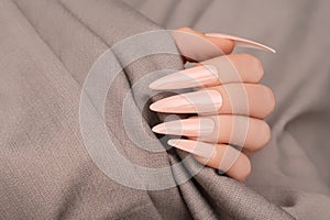 Female hand with long rose nail design. Long nail polish manicure. Woman hand on beige fabric background