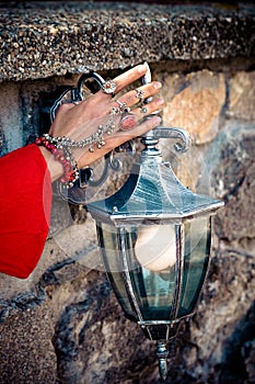 Female hand with a lot of oriental boho jewelery on lantern outdoor against stonewall