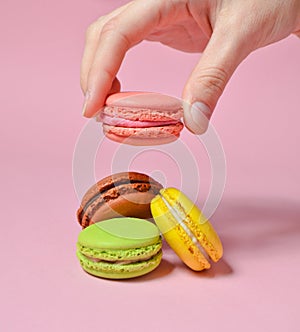 Female hand lowers the pink macaroons cookies. Many macaroons on a pink pastel background. Minimalism.