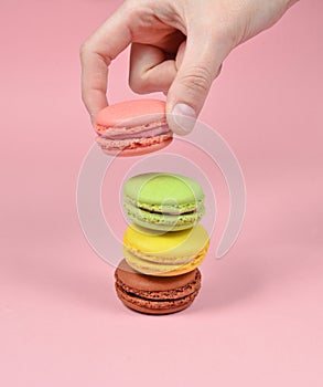 Female hand lowers the pink macaroons cookies. A stack of macaroons on a pink pastel background.