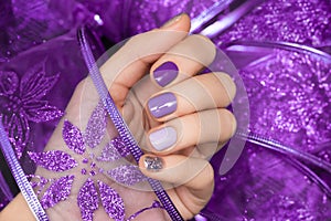 Female hand with magic nail design. Glitter purple nail polish manicure. Female hand hold purple lace fabric