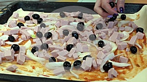 Female hand with manicure throws olives on the pizza on the table