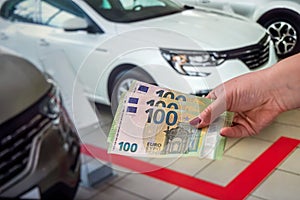 female hand with manicured red nails holds a large amount of euro banknotes near the car