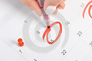 Female hand marking with a red pen on a 15th day of the month  calendar circles the day, deadline concept