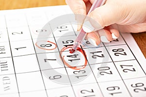 Female hand marking with a red pen on a calendar circles the 14 day, deadline concept