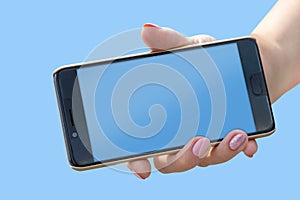 Female hand with a mobile phone on a blue background. Isolated. Copy space.