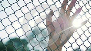 Female hand moving along the surface of grid. Arm of young woman touching metal wire fence. Girl walking during summer